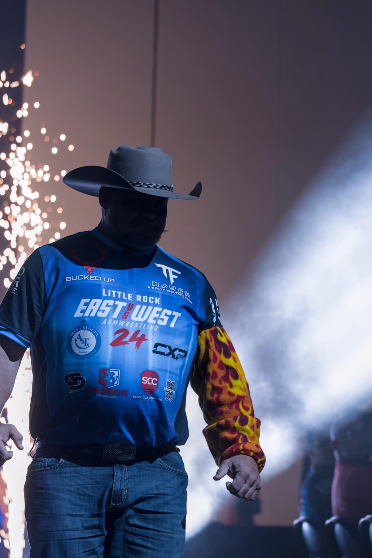 East vs West 24: a competitor in a cowboy hat walks to the table through sparks and smoke